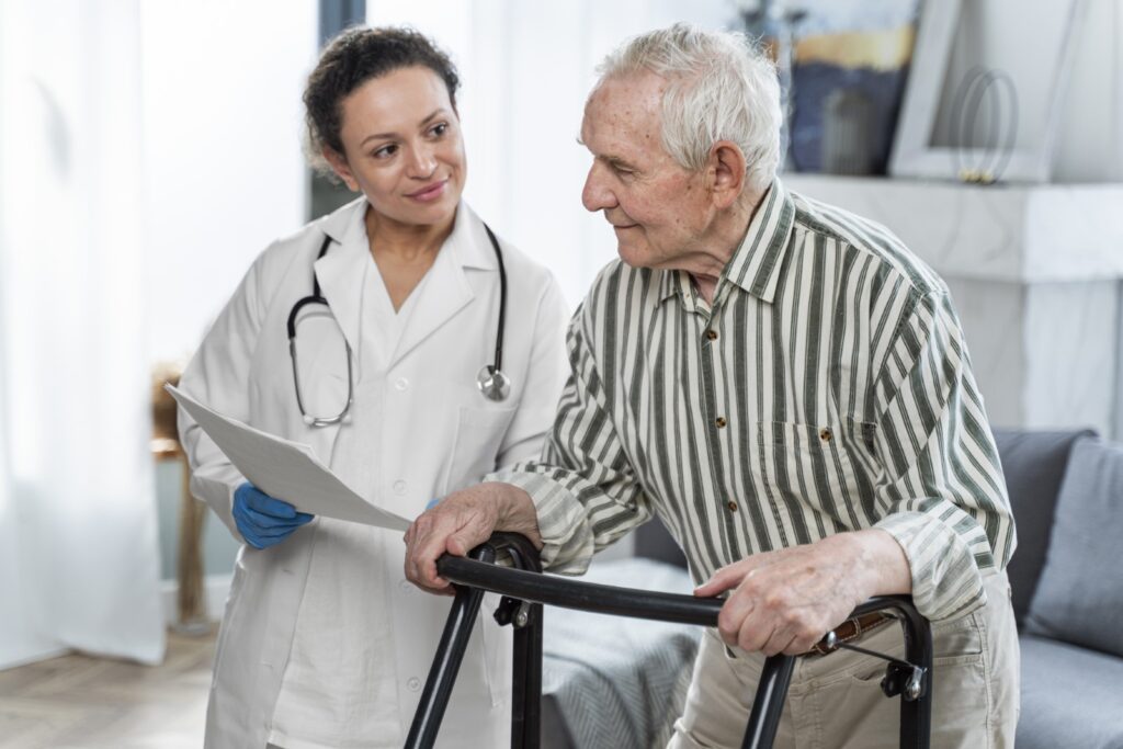 Como cuidar de idosos: Na imagem, idoso se apoia em andador e tem acompanhante da área da saúde ao seu lado.